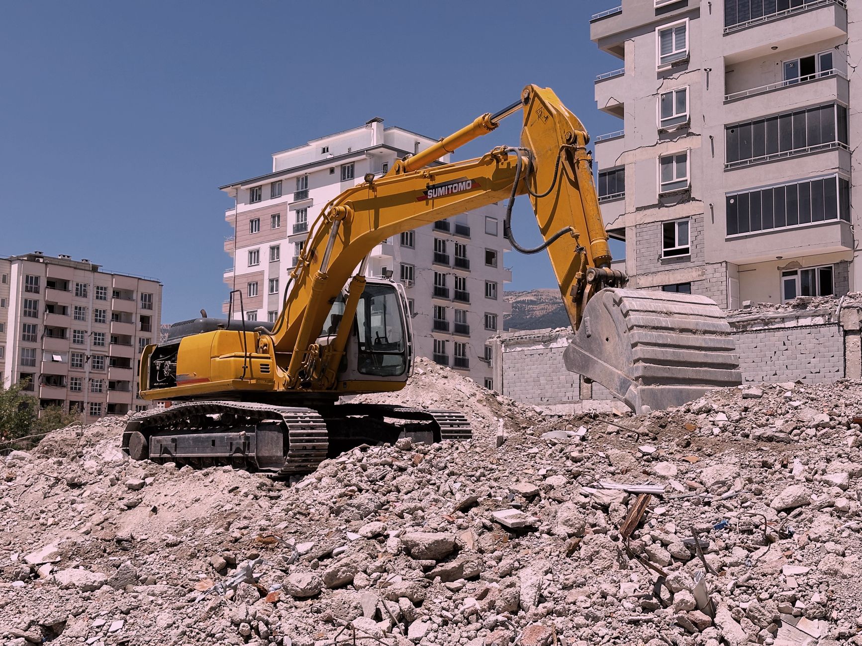 Yellow excavator working on an urban construction site amidst rubble and buildings.